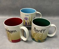 Front and side views of the three Starbucks mugs featuring Copenhagen, Dubai, and Banff, showing colored interiors and city/animal themed designs.
