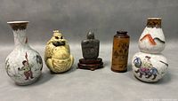 Front view of all five items showing the porcelain crackle bud vases at either end, carved ivory erotic snuff bottle second from left, dark stone snuff bottle with wooden stand center, and wooden painted snuff bottle second from right.