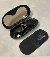 Pair of gold-tone framed Carrera Porsche Design sunglasses with tinted lenses and black protective case with inside semi-transparent lens-shaped shading, also showing soft black pouch with Carrera Porsche Design logo on surface.