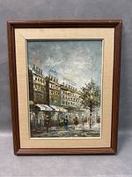 Front view of framed oil painting depicting street scene with multiple buildings and pedestrians
