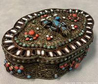 Closed view of Tibetan brass filigree trinket box showing intricate design and colored stones.