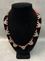Front view of the Tibetan necklace displaying the silver pendants and red coral beads on a black display stand.
