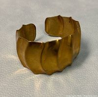 Close-up image of vintage Claude Abittan signed cuff bracelet showing the textured ridged wave design and open cuff shape on a white textured surface.