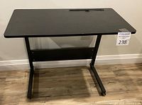 Front view of the black adjustable height table showing the flat top surface and front legs with feet on wheels.