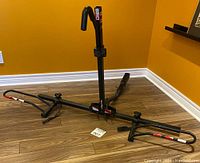 Front angled view of black SportRack single bike rack showing frame support arms and vertical upright with hooks.
