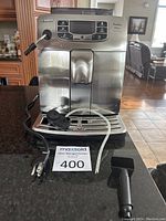 Front view of machine on countertop with power cord, milk tube, drip tray and scoop/tamper placed in front