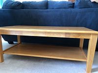 Full view of rectangular solid pine wood coffee table with flat top and lower shelf, positioned in front of a blue couch on carpet.
