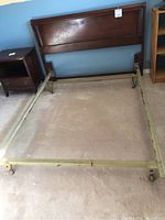 Full view of metal bed frame with caster wheels and attached wooden headboard.