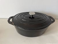 Black oval cast iron Dutch oven with lid showing a small chip on lid edge and metal knob.