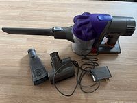 Full view of Dyson handheld vacuum with three attachments and power cord charger on wooden surface