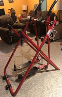Red Gazelle foldable elliptical exerciser positioned on carpeted floor near sitting area.