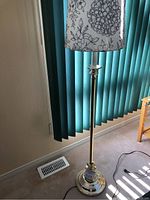 Full view of floor lamp showing the lamp base, stand and floral fabric lampshade with gray flowers on a white background.