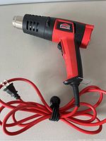 Side view of Jobmate heat tool showing red and black body, vented metal nozzle, and attached red power cord coiled with a black strap.