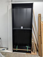 Tall black Ikea bookshelf against a white wall with one shelf installed and green tape at the bottom, showing the full height and width of the unit.