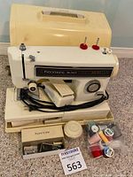 Kenmore Ultra Stead II sewing machine with power cord, control dials, two red spool holders, and assorted sewing threads and accessories on a beige tray.