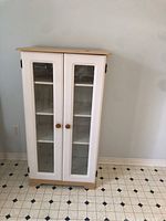Front view of wooden storage cabinet with glass panel doors, showing two doors with wooden knobs and a natural wood top.