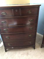 Front view of tallboy dresser showing five large drawers with oval brass pulls and two smaller top drawers with one keyhole visible.