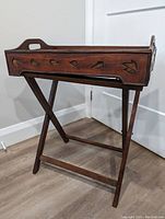 Side view of assembled wooden tray on folding stand showing carved leaf designs on tray sides and cut-out handles.