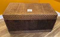 Closed brown wicker trunk with woven exterior and rectangular shape.