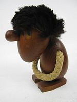 Side view of the teak troll figurine showing its profile, fur hair, braided rope, and wooden nose.