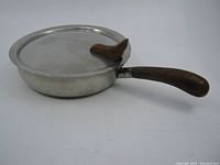 Full side view of the round stainless steel cooking pot with lid and curved rosewood handle.