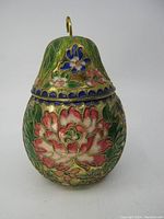 Front view of the pear shaped cloisonné lidded box showing detailed floral enamel patterns in pink, blue and green with a brass stem handle.