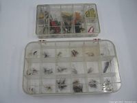 Clear view of two plastic boxes with compartments filled with various fishing flies and lures, viewed from above.