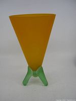 Front angle photo of the old handmade glass vase showing its frosted orange conical triangular body and green tripod base.
