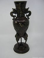 Front angle view of dark bronze urn showing decorative birds and lotus flower pattern, dragon handles, and tripod legs on round base.