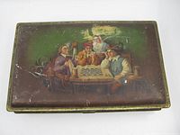 Top view of the rectangular metal tin featuring painted artwork of four 18th-century style characters playing chess, showing overall wear and scratches.