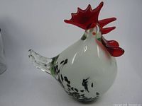 Side view of the Murano glass rooster showing white body with black spots, red comb and wattles, and clear tail.