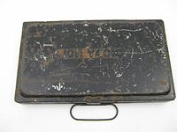 Top closed view of metal paint box with heavy wear and orange name stenciled Jon Yeo.