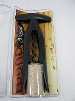 Top-down view of black Screwpull corkscrew with helical screw inside clear plastic case showing printed branding and background card.