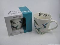 Photo showing one hummingbird-themed coffee mug and its original box packaging, highlighting the artistic design and branding