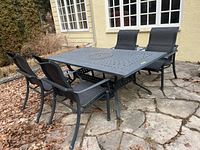 Full view of outdoor metal patio set showing table and four matching chairs on stone patio.