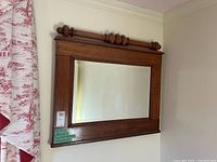 Front view of wood-framed mirror with rectangular bevel glass and decorative turned wood accents on top.