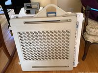 Two plastic expandable baby gates stacked together. Both are white with ventilation holes and handles at top center. One includes a visible locking mechanism.