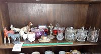 Several horse and dog figurines, glass jars, crystal candy dishes, and other decorative items on a wood shelf