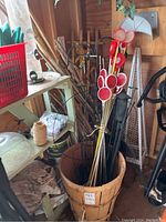 Photo showing a wooden basket filled with red and white reflective markers on stakes, bamboo stakes, black metal garden hooks, and a black garden torch.