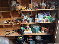 Wide view of wooden shelves containing assorted garden tools, fertilizers, small pots, bags of fertilizer, garden gloves, and sprayers