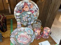 Overall set showing floral candle holders, plates, bowl, shakers with coasters, and crystal figurine on a shelf