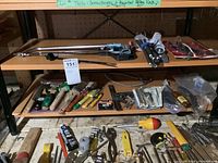 Wide view of multiple shelves with hand tools such as screwdrivers, tape measure, wrenches and small hardware kits arranged on them.