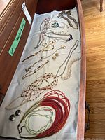 Top view of drawer containing necklaces, bracelets, earrings, and chains in various designs and materials arranged on white fabric.