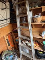 Weathered metal extension ladder resting vertically in a corner with climbing rungs visible
