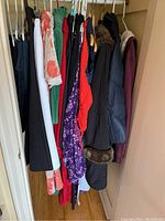 Full view of ladies clothing on hangers showing various tops, dresses, pants, and a padded coat with fur trim on hood.