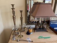 Photo showing table lamp with fabric lampshade and two sculpted bird figures on base, along with three brass candle holders, two candle snuffers, glass tealight holder, and metal candle holder container with lid and tassel