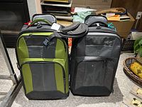 Two upright Eagle Creek rolling suitcases side by side, one green/gray and one black/gray, shown from front.