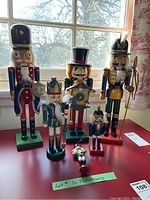 Group view of five hand-painted wooden nutcrackers alongside a small nutcracker tree ornament. Different sizes and traditional festive uniforms are visible.