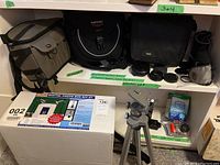 Photo showing the digital photo box kit packaging, three camera bags, lens covers and other accessories arranged on shelves.