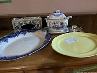 Photo of the full lot showing the platters, soup tureen, Kleenex box, and small silver creamer on a wooden surface.